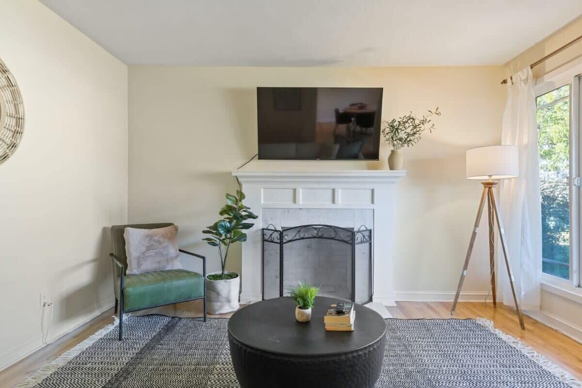 Una sala de estar con chimenea, televisor montado arriba, un sillón, una mesa de centro y una lámpara de pie.
