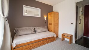 Een slaapkamer met een bed, een houten garderobe, een klein houten tafeltje en een wandlamp.