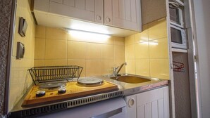 Een kleine keuken met een fornuis, spoelbak en een magnetron boven het aanrecht.
