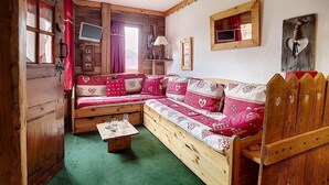 Een gezellig, chalet-achtig vertrek met een banksofa van hout, een kleine tafel en een houten deur.