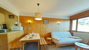 A cozy room with a wooden interior, a dining table with benches, a sofa, and a small table with a lamp.