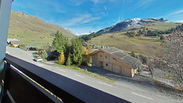 A view from a window overlooking a rural landscape with a house, a road, and mountains in the distance.