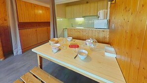 A wooden kitchen with a wooden table set for dining, a hanging light fixture, and wooden cabinets.
