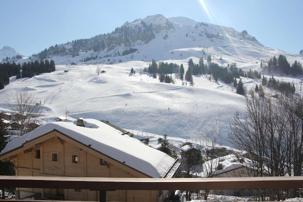 Une vue sur une montagne, avec un paysage enneigé, un bâtiment en bois doté d’un toit en pente et un ciel dégagé.