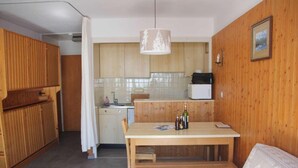 A compact kitchen with wooden cabinets, a dining table, and a hanging light fixture.