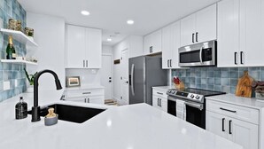 Une cuisine moderne avec des meubles blancs, un évier noir, un réfrigérateur en acier inoxydable, un four à micro-ondes et une cuisinière.