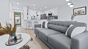 Une cuisine moderne avec des meubles blancs, un canapé gris et un coin repas équipé de tabourets.