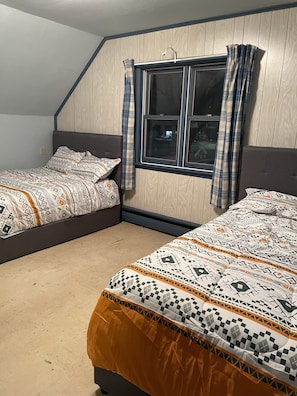 A bedroom with two beds, a window with curtains, and a sloped ceiling.