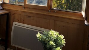 En stuga av trä med ett stort fönster som vetter ut mot ett bergigt landskap, en flagga och ett bord med en vas med blommor.