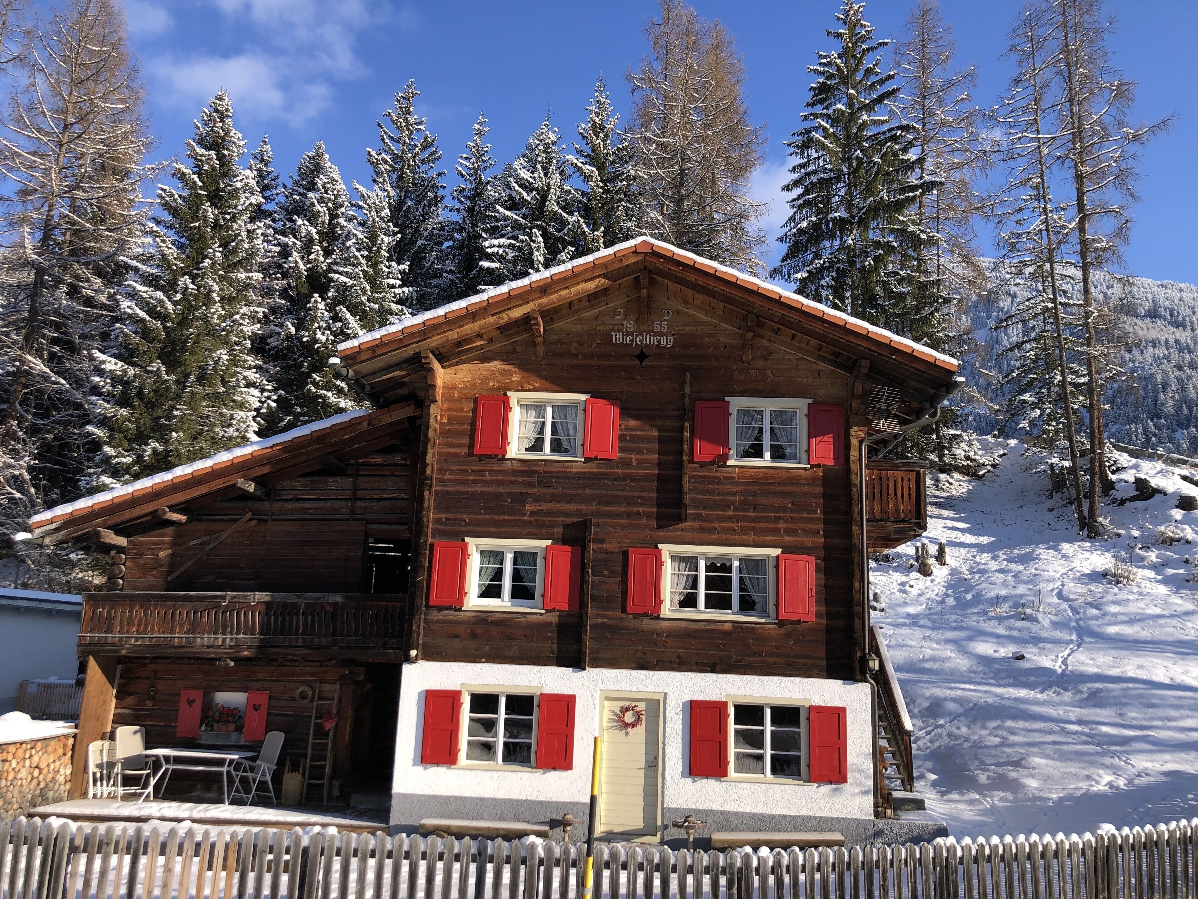 A wooden chalet with red shutters, a balcony, and a stone wall.