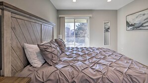 Une chambre à coucher avec un grand lit, une tête de lit en bois, une fenêtre donnant sur un beau paysage et une œuvre d’art encadrée accrochée au mur.