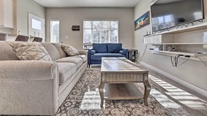 Un salon avec un canapé, une table basse, un téléviseur fixé au mur et un tapis à motifs.