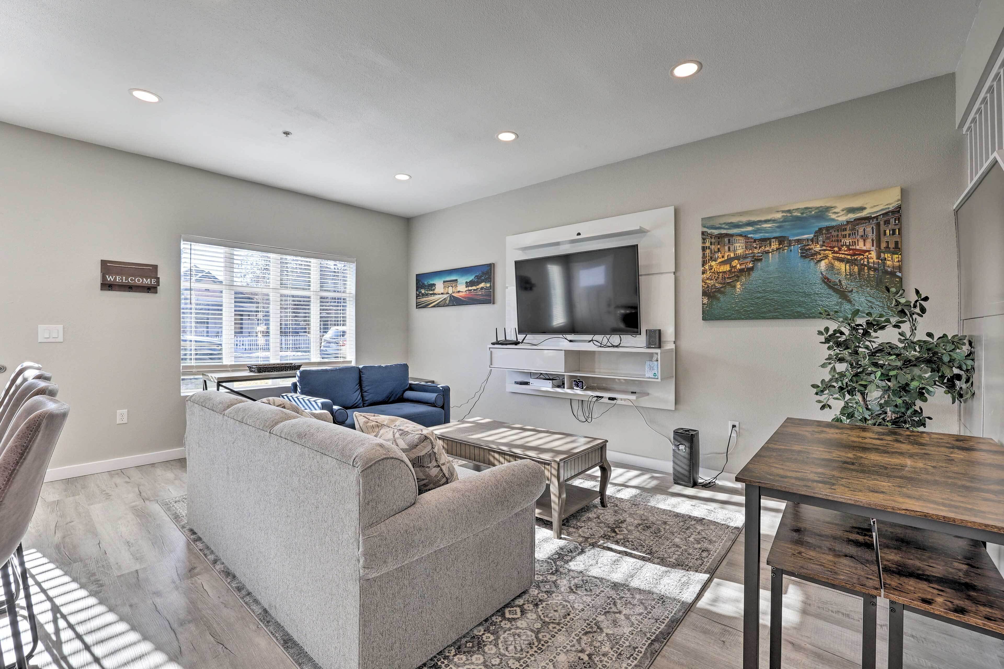 A modern living room with a grey sofa, a coffee table, a TV mounted on the wall, and a cityscape painting.