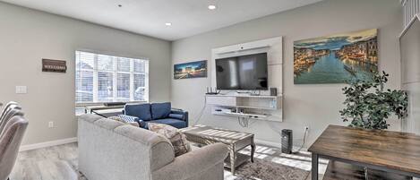 A modern living room with a grey sofa, a coffee table, a TV mounted on the wall, and a cityscape painting.