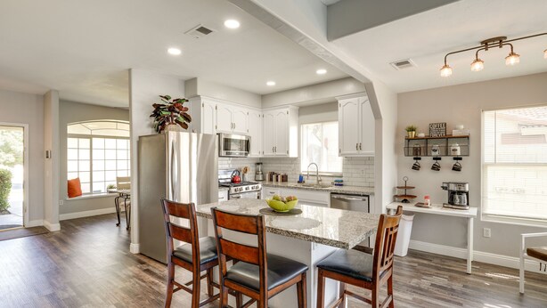 Una cocina moderna con armarios blancos, una isla central y un comedor con sillas de madera.