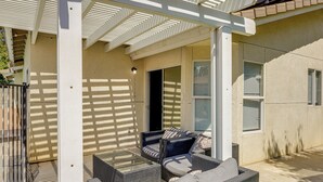 Un patio cubierto con mobiliario de mimbre, una mesa de vidrio y una puerta que da al interior.