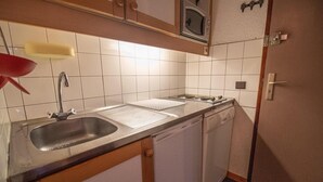 Pieni, käytännöllinen keittiö, jossa on pesuallas, kaksi keittolevyä, mikroaaltouuni ja astianpesukone.