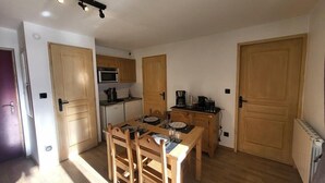 A compact kitchen with wooden cabinets, a microwave, a coffee maker, and a dining table with chairs. - 10m from resort center, 1st floor, terrace, tv, ski locker, 26m², Montgenèvre (Montgenèvre)