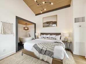 A bedroom with a large bed, a built-in bathtub, a wooden ceiling, and a wall-mounted picture.