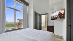 Habitación de hotel con una cama grande, un televisor montado en la pared y vistas a un edificio.