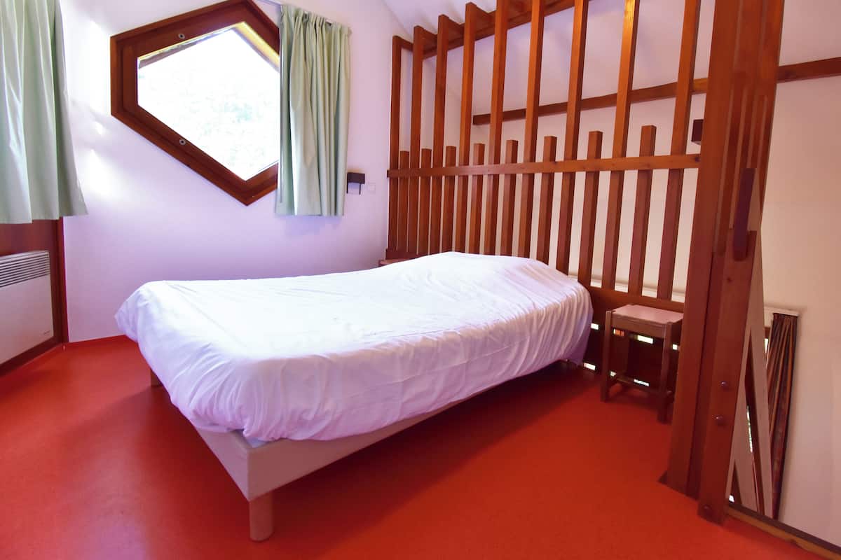 A bedroom with a bed, a window, and a wooden slat wall.