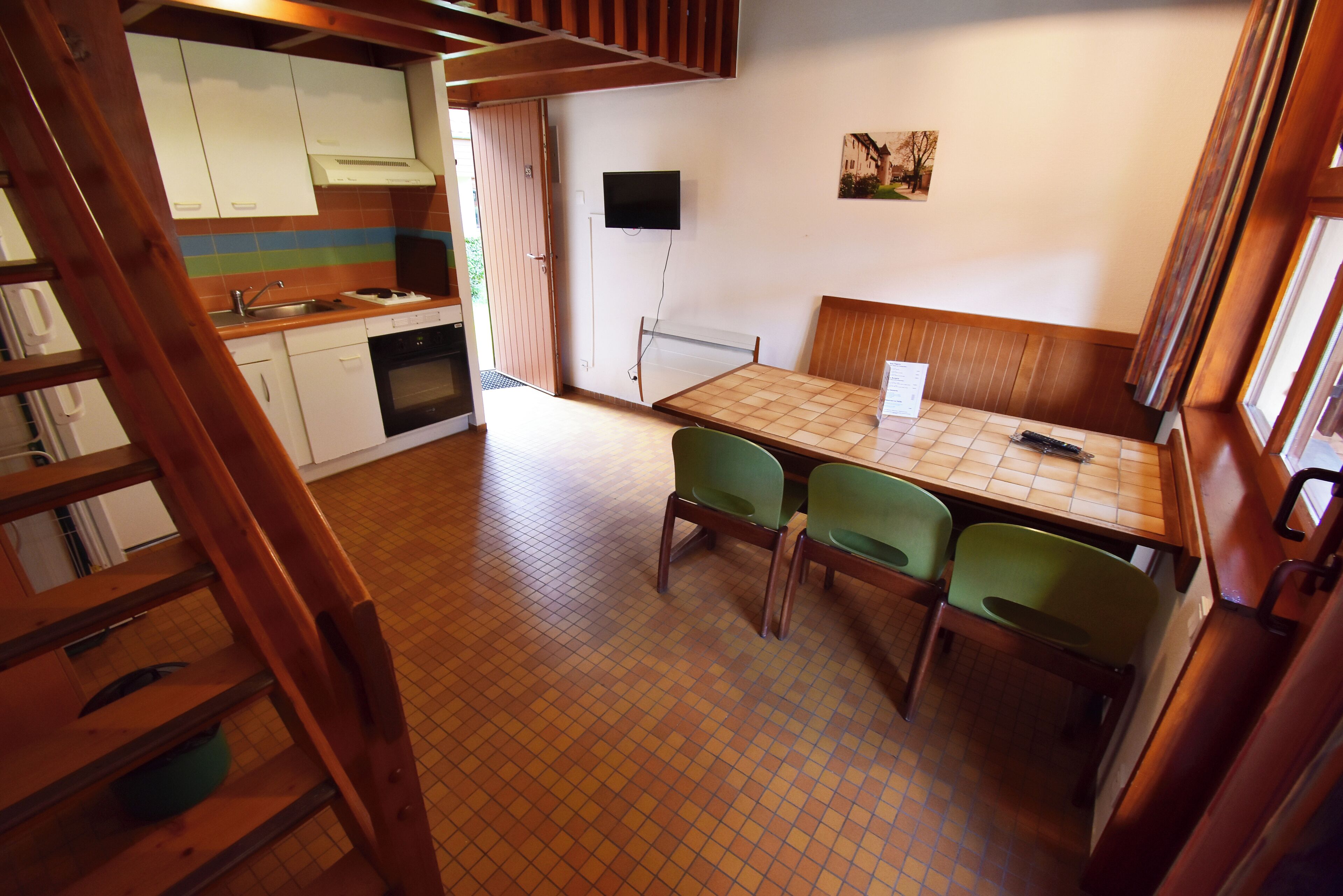 Een compacte keuken met een eethoek, een aan de muur bevestigde televisie en een houten tafel met stoelen.
