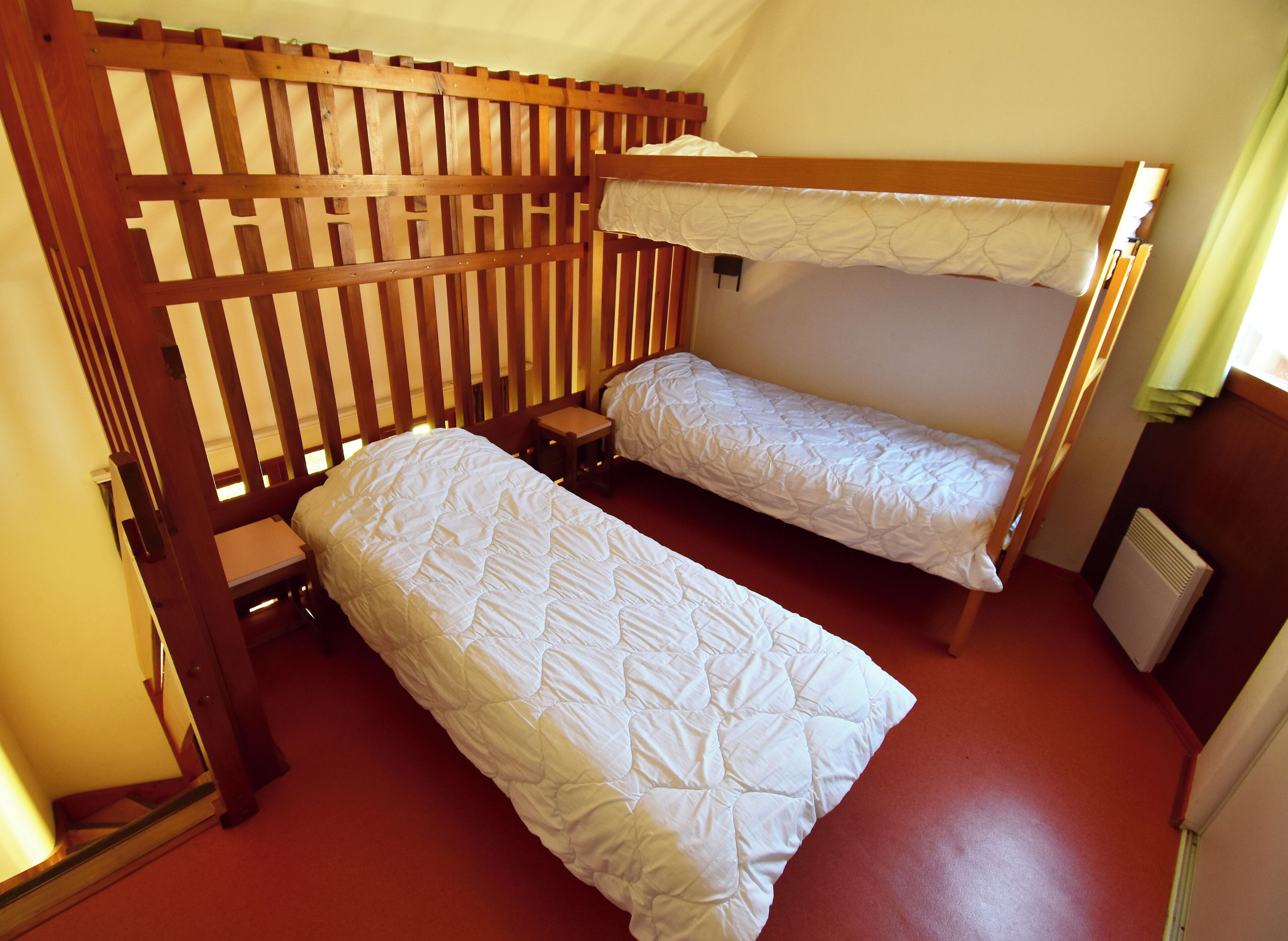 Quarto tipo dormitório com duas beliches, uma mesinha e um radiador.