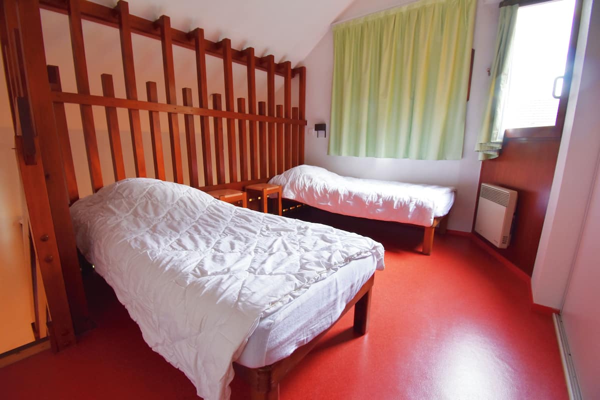 A room with two beds, a wooden headboard, a window with green curtains, and a red floor.