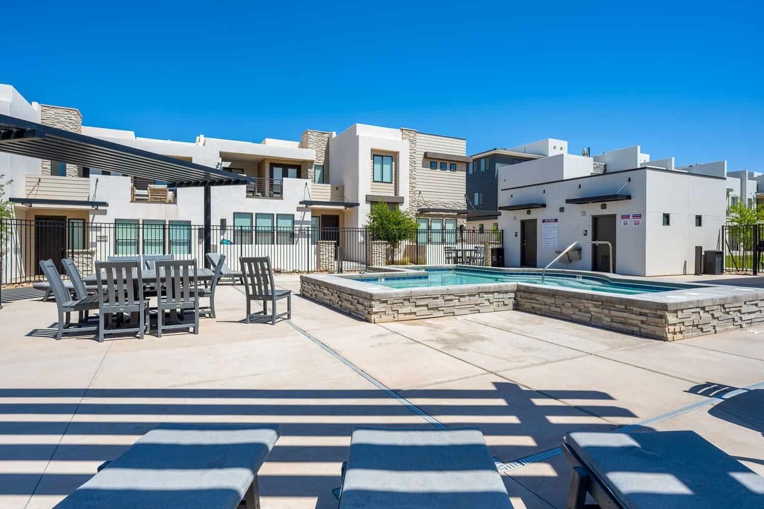 Un moderno edificio residencial con piscina, mobiliario exterior y un patio cubierto.