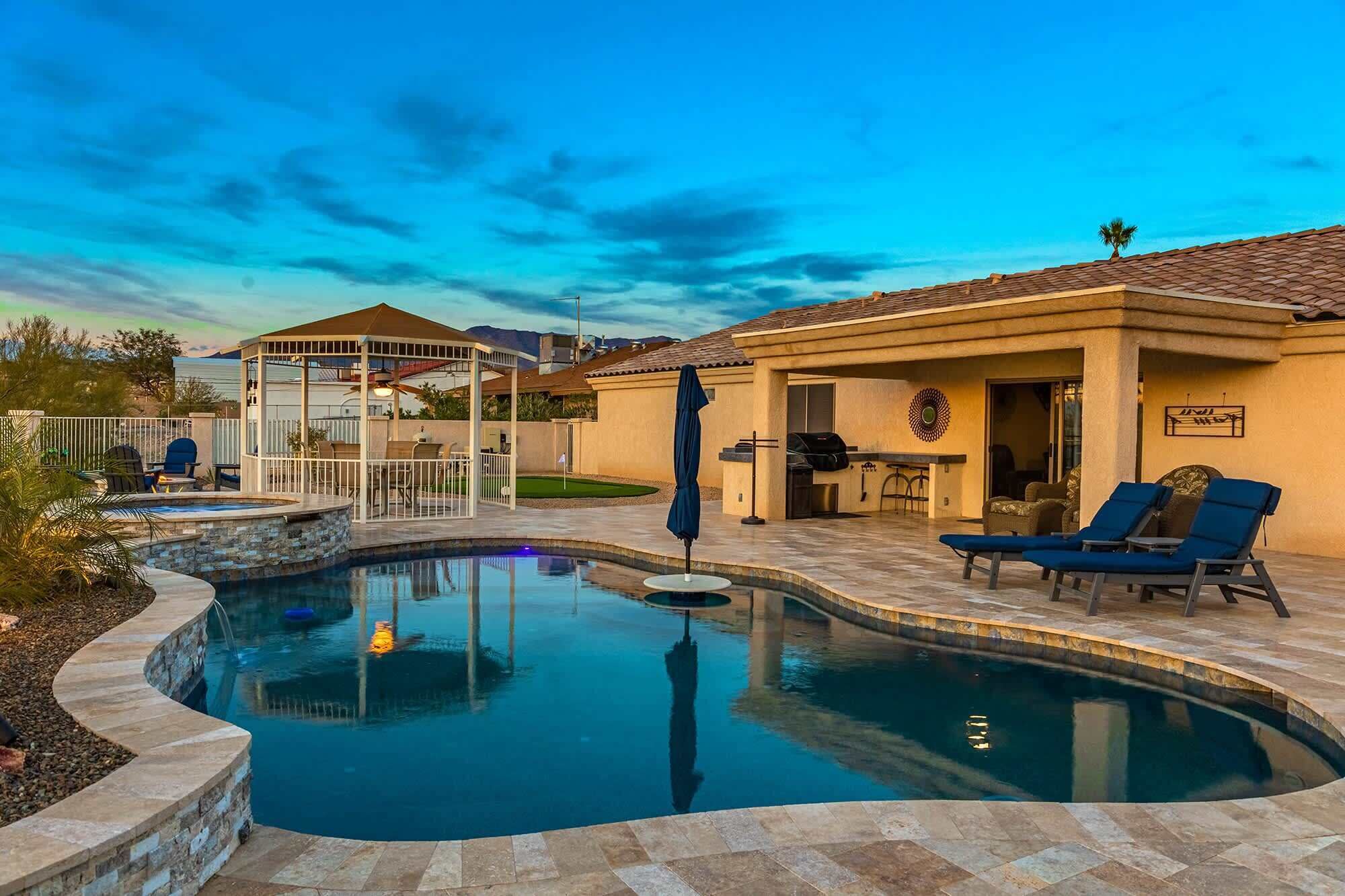 Ein Pool mit geschwungener Form, ein überdachter Sitzbereich und eine Grillanlage.