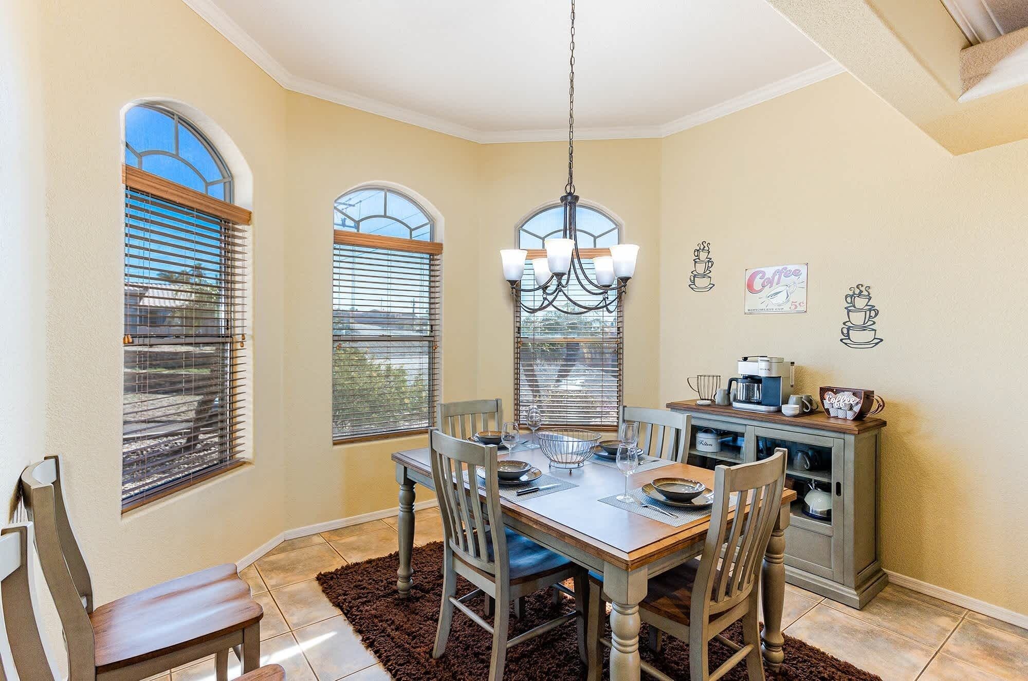 A dining area with a table, chairs, a chandelier, and a coffee station.