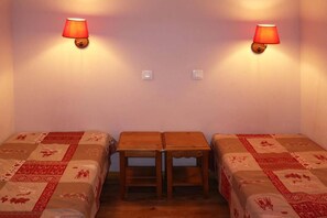 A room with two single beds, a small table, and two wall-mounted lamps.