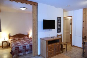 A bedroom with a bed, a TV mounted on the wall, a wooden desk, and a chair.