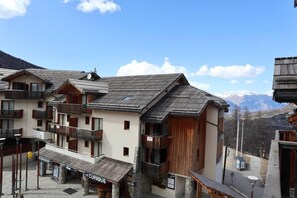 A mountain resort with chalet-style buildings, balconies, and a restaurant named 'Le Curieux'.