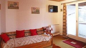 A cozy room with a wooden sofa, a small table with a red cloth, a TV mounted on the wall, and a sliding glass door leading to an outdoor area. - 250m from shops, 3rd floor, view valley, balcony, 30m², Les Orres (Les Orres)