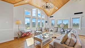 A spacious living room with a high ceiling, large windows, and a view of the beach. - Luxury Semi-Oceanfront Home w/ Pool, Elevator, Theater Room, and Game Room (Hatteras)