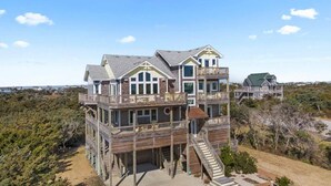 A large, multi-story beachfront house with multiple balconies and a covered front porch. - Luxury Semi-Oceanfront Home w/ Pool, Elevator, Theater Room, and Game Room (Hatteras)