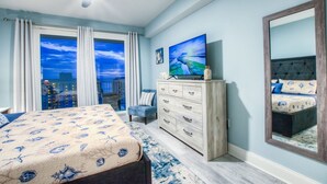 Ein Schlafzimmer mit einem großen Bett, einem Schminktisch, einem Fernseher und Blick auf die Stadt durch das Fenster.