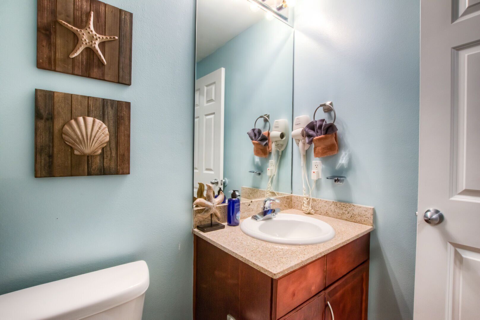 A bathroom with a wooden vanity, a white sink, and a mirror. There are two seashells on the wall and a starfish decoration.