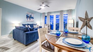Ein modernes Wohnzimmer mit einem blauen Sofa, einem Esstisch für zwei Personen und einem Blick auf die Stadt durch große Fenster.
