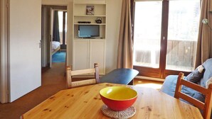 Ett rum med ett träbord, en röd och gul skål, en blå stol och en säng i bakgrunden.