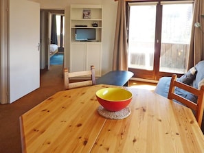 A wooden dining table with a red and yellow bowl in the center, a blue chair, and a view of a balcony through a window.