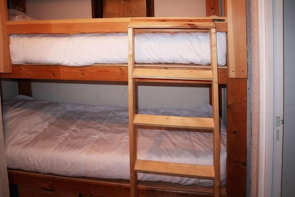 A bunk bed with a wooden ladder, white bedding, and a wooden headboard.