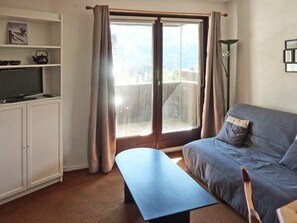 A living room with a sofa, a bench, a TV, and a sliding glass door to a balcony.