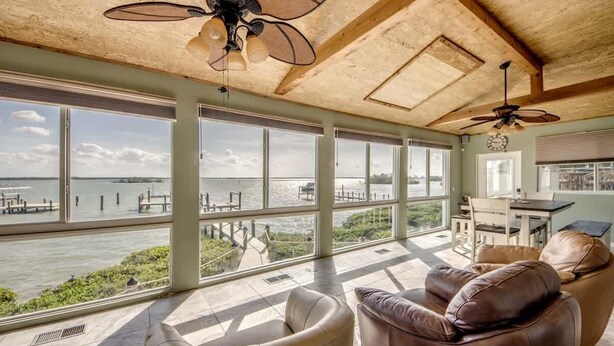 A spacious room with large windows, a ceiling fan, a dining area, and a view of the water. - 21431 Widgeon Bayfront Pool Home near the Beach (Fort Myers Beach)