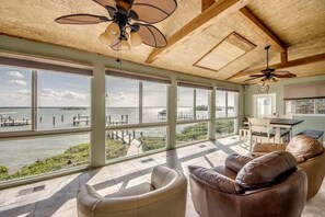 A spacious room with large windows, a ceiling fan, a dining area, and a view of the water.