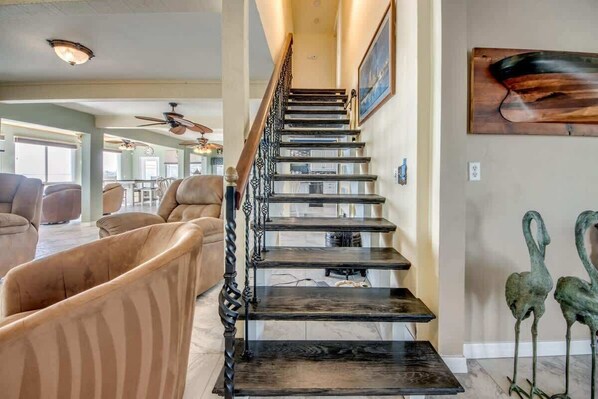 A staircase with a dark wooden finish and ornate metal railings, leading to a living area with leather sofas and a dining table. - 21431 Widgeon Bayfront Pool Home near the Beach (Fort Myers Beach)
