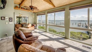 A spacious living area with a large window overlooking a marina, a ceiling fan, and a leather sofa. - 21431 Widgeon Bayfront Pool Home near the Beach (Fort Myers Beach)