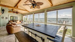 A spacious room with a large wooden table, a ceiling fan, and a view of the water. - 21431 Widgeon Bayfront Pool Home near the Beach (Fort Myers Beach)