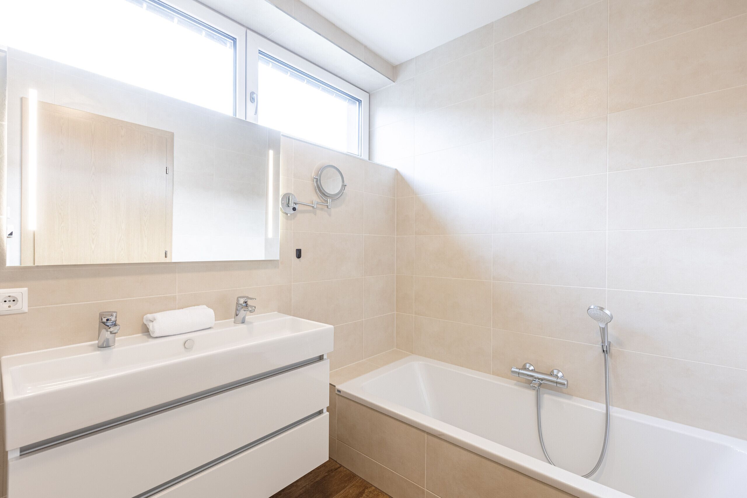 A modern bathroom with a bathtub, a vanity with a mirror, and a window above the mirror.